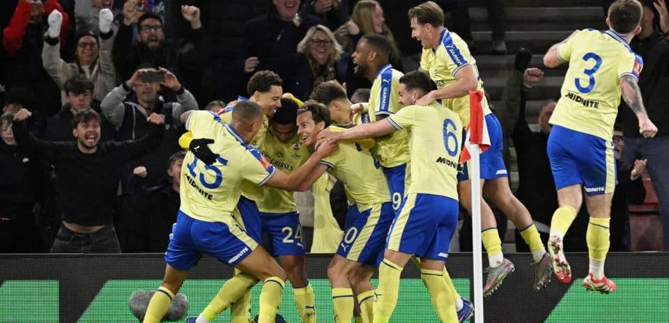 Jugadores celebrando un gol con aficionados animando