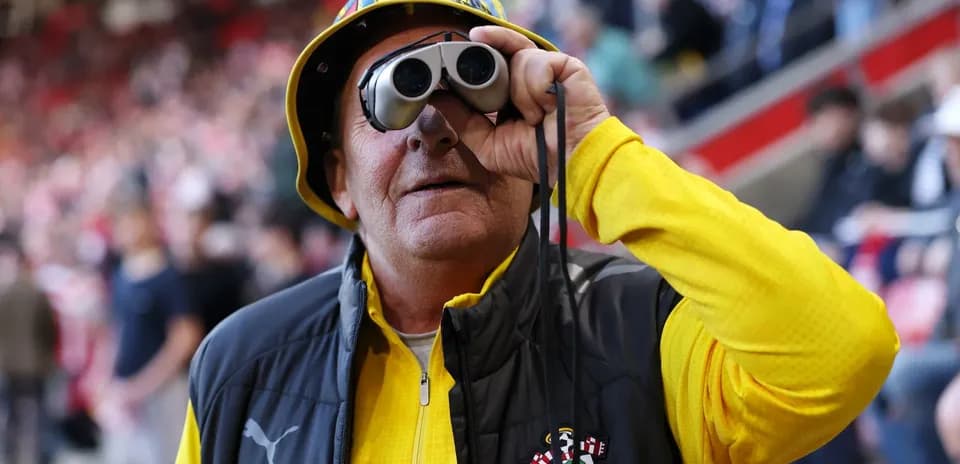 A fan with binoculars wearing a yellow hat