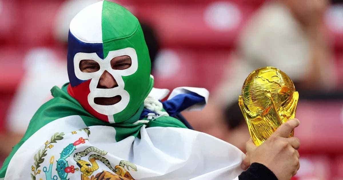 A fan wearing a mask holding the World Cup trophy