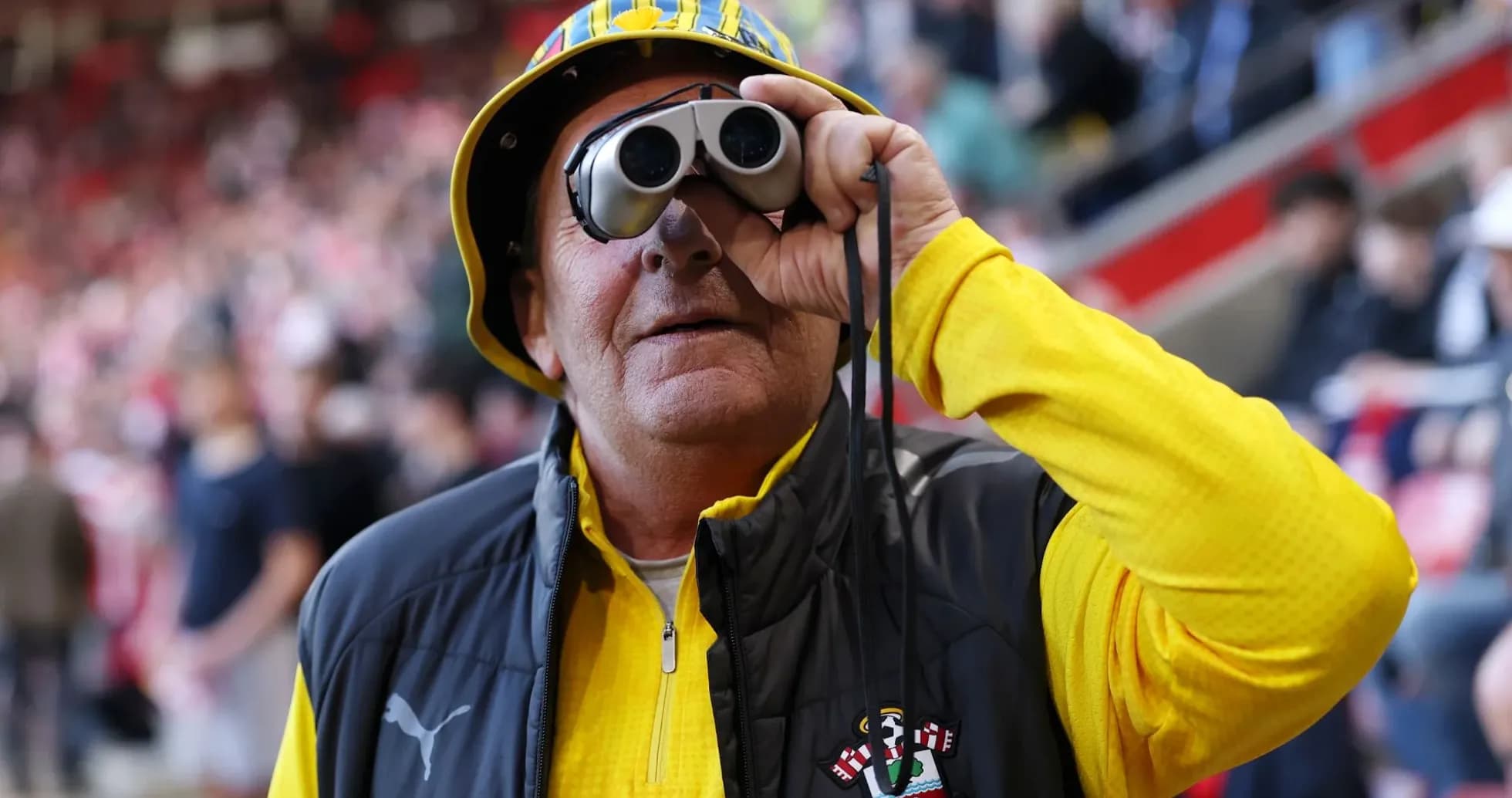 A fan with binoculars wearing a yellow hat A fan with binoculars wearing a yellow hat